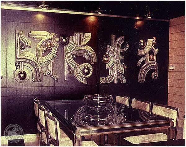 Wall sculptures displayed in a dining room: pairs of gold relief panels with abstract Hebrew-letter-like forms and spheres, mounted on dark walls.