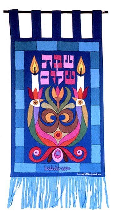Tapestry 'Shabbat Shalom': two Sabbath candles flanking Hebrew text above a symmetrical floral owl-like emblem in maroon, blue and green, blue fringed border.